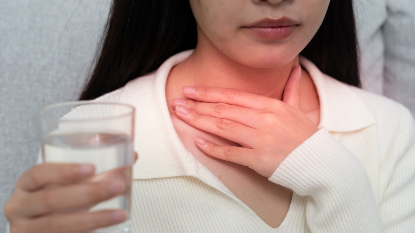 Mujer sosteniendo la garganta con molestia, con un vaso de agua en la otra mano